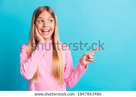 Photo portrait of amazed schoolgirl pointing showing blank space touching cheekbone smiling isolated on bright turquoise color background