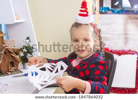 A little cute girl holding a large paper cut snowflake in her hands Christmas mood, early development, a child in a Santa Claus hat, preparing for the new 2021.