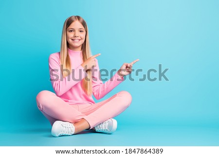 Photo of cheerful nice blond teen girl sit lotus point empty space dress pink pants poloneck isolated on teal background