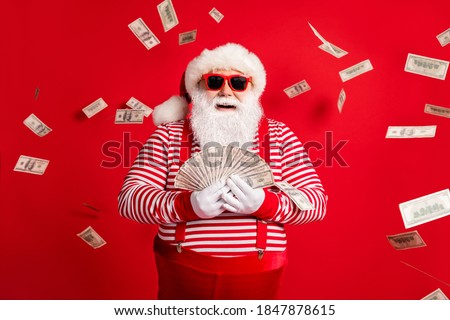 Photo of retired old man grey beard hold cash fan newyear shopping season wear santa costume suspenders sunglass gloves striped shirt headwear isolated red color background