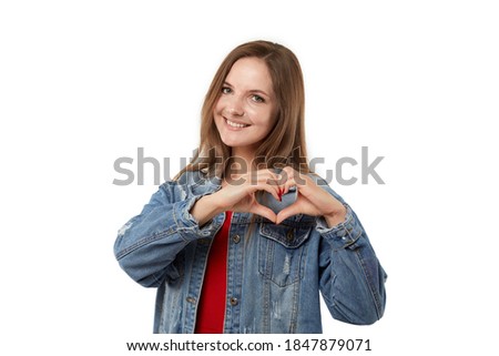 Cute funny young woman shows heart and love sign. In a denim jacket. White isolated background.