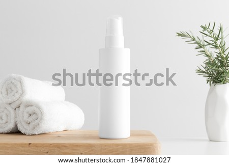 White cosmetics lotion bottle mockup with towels and a rosemary on a wooden table.
