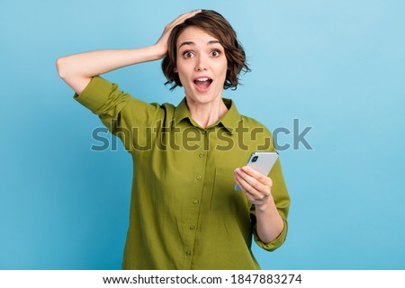 Photo of charming cute lady short hairdo hands hold telephone arm head open mouth amaed look camera wear green shirt isolated blue color background