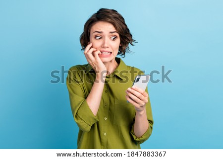Photo of horrified lovely lady short hairdo arms hold telephone gnaw bite nail horrified look screen wear green shirt isolated blue color background Royalty-Free Stock Photo #1847883367