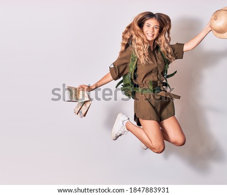 Young beautiful blonde backpacker girl wearing backpack smiling happy. Jumping with smile on face holding city map and hat over isolated white background