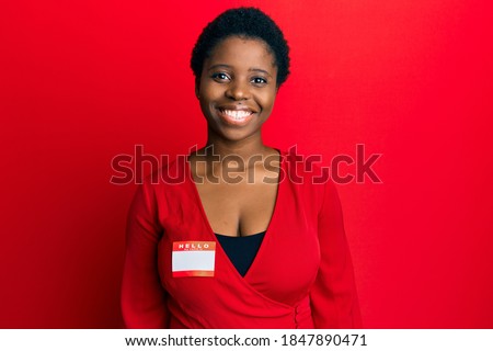Young african woman with short hair wearing hello my name is sticker identification looking positive and happy standing and smiling with a confident smile showing teeth 