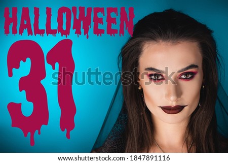 woman with black makeup and veil looking at camera near halloween 31 lettering lettering on blue