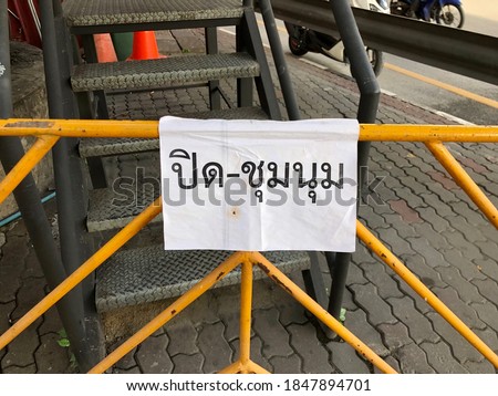 The yellow metal barricades on the street in Bangkok, with white sheet of paper hangs on it. The Thai words on the paper is “Block the protesters”