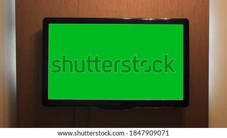 Green screen TV hanging on wall. Concept. Home TV with green screen on wall of house. Plasma TV with wide screen and green background