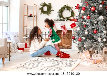 Cute African-American girl and her mother near fireplace at home on Christmas eve