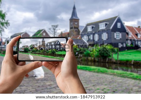 Tourist taking photo of traditional wooden fishing houses, canal and cat in Marken, Netherlands. View of canal, bridge and traditional wooden fishing houses in waterland village. 