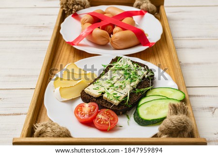 Useful and unhealthy food concept. A plate with tasty and healthy food made from cheese and vegetables next to a crossed out plate of sausage.