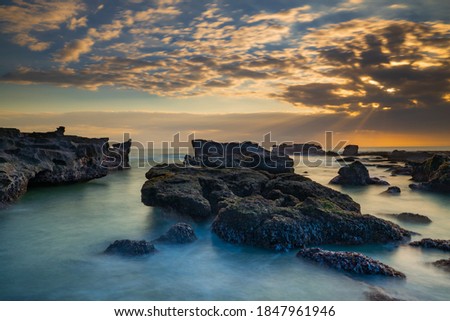 Beautiful seascape. Long exposure rocky beach during low tide. Panoramic ocean view. Composition of nature. Sunset scenery background. Cloudy sky. Water reflection. Mengening beach, Bali, Indonesia