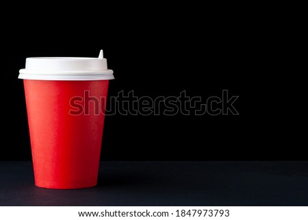Red cup of coffee with a white cap on a black background. Recycled and recyclable coffee paper cup. Copy space and horizontal orientation. 