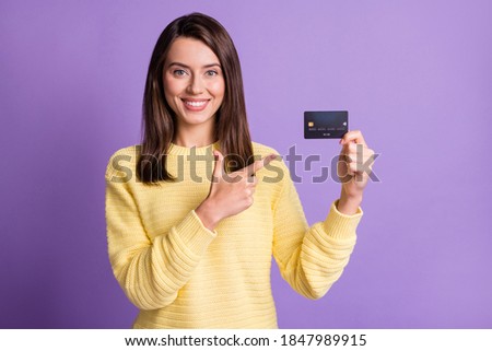 Photo portrait of beautiful girl wearing yellow sweater pointing on credit card with finger smiling isolated on bright purple color background