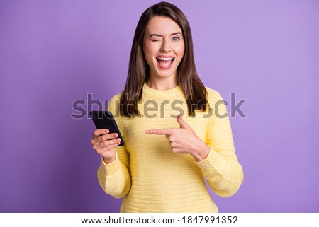 Photo portrait of woman holding phone in one hand pointing finger winking with eye open mouth isolated on vivid purple colored background