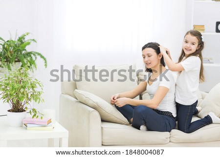 Photo of smiling mom with short dark hair and her beautiful little daughter who is brushing her hair.
