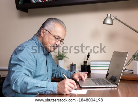 Senior man learn to use computer. Old man in glass and blue shirt using a laptop computer for online studying at home office Royalty-Free Stock Photo #1848004198