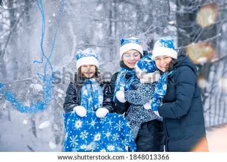 Portrait of a happy family of mother and  her children in a winter decorated forest. The children are in a dark coat,  blue  Santa Claus hat, scarf and mittens. Family christmas new year.
