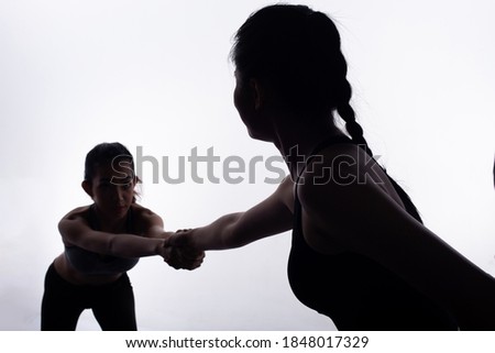 Silhouette slim body of two Young Fitness Women pull hands each other and friend support as coach, they cheer up to go. High contrast white background copy space