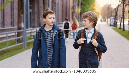 Caucasian happy nice male school students walking on street after school and chatting. Portrait of joyful young boys pupils with backpacks in good mood speaking outdoors in city. Classmates concept Royalty-Free Stock Photo #1848033685