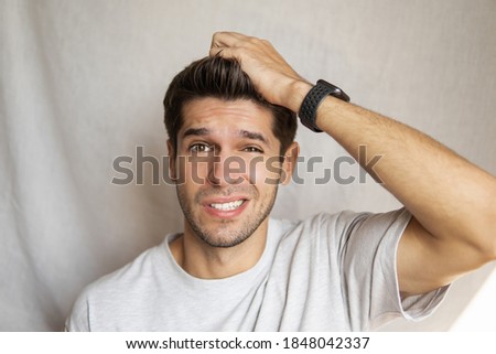 Portrait of a charming young man with a confused face expression and his hand on top of the head 