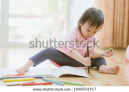 Little asian girl having fun on floor, girl was coloring cartoons on coloring book at home. Coloring Book Education Talent Concept. Copy space.