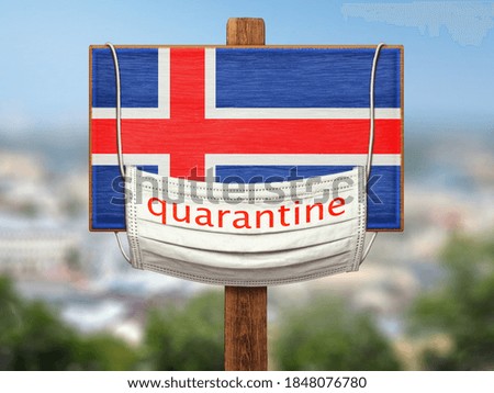 The sign on the background of the city. Quarantine during the COVID-19 pandemic in Iceland. A medical mask with the words "Quarantine" hangs on a tablet with the flag of Iceland. Limitations.
