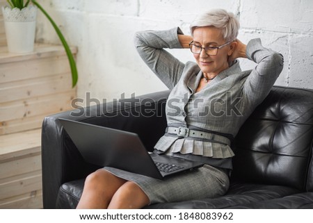 beautiful stylish adult woman in suit working with laptop on black sofa