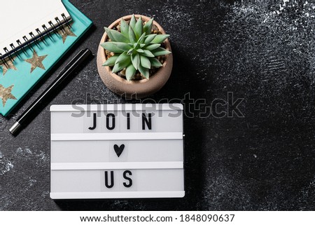 Join Us text on the lightbox on black office desktop with notebooks, pen and succulent flower, copy space for your design. Concept of hiring and recruitment. 