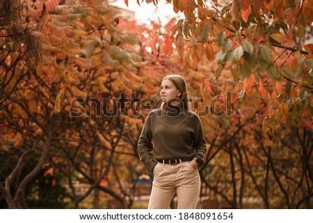 Young beautiful girl dressed in stylish clothes, green sweater and beige pants, in an autumn park with beautiful trees