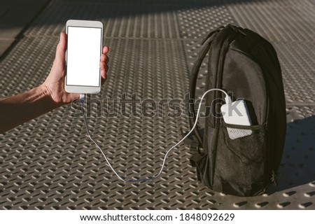 Mock up of a smartphone in a man's hand. Charging from a power bank in a backpack pocket