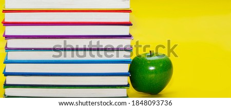 Green apple next to colorful stack of books on yellow background