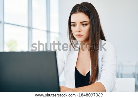Pretty businesswoman sitting at her desk working on laptop in modern office. Business professionals. 