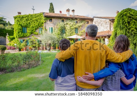 Back view of happy family hugging is standing outside their new house - This photo canuse for family, father, mother and home concept