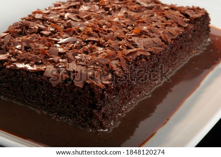 Big brownie cake soaked in chocolate syrup, with shredded chocolate on top as garnish, on a white platter. Royalty-Free Stock Photo #1848120274