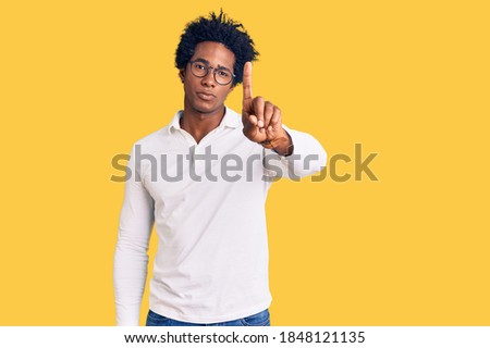 Handsome african american man with afro hair wearing casual clothes and glasses pointing with finger up and angry expression, showing no gesture 