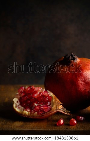 A quarter of a pomegranate in front of a partial view of a whole pomegranate in dark tones