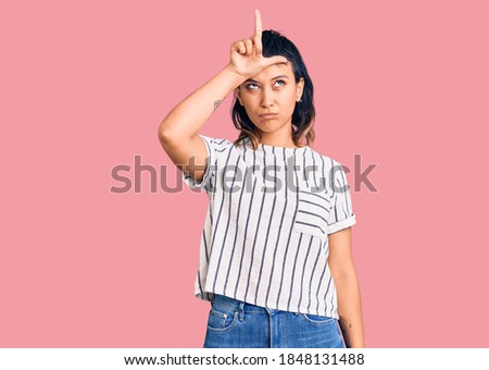 Young woman wearing casual clothes making fun of people with fingers on forehead doing loser gesture mocking and insulting. 