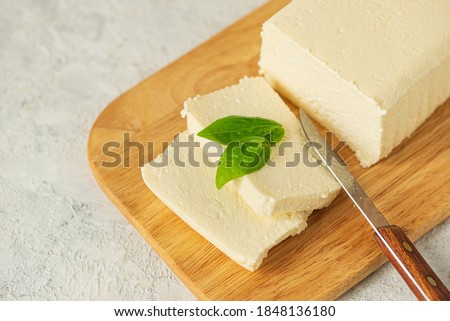 tofu, paneer, soy cheese, curd cheese, brynza, feta, Adyghe cheese with Basil and a knife on a wooden cutting Board on a light background Royalty-Free Stock Photo #1848136180