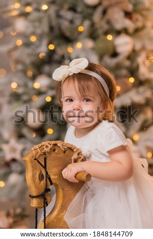 Close-up portrait of a little girl riding a horse on a wooden vintage rocking chair against the background of a Christmas tree. Christmas and New Year. Holiday concept. Selective focus