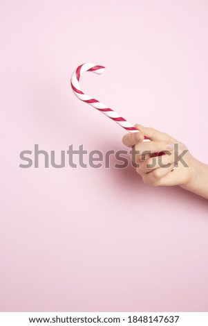 Female hand holding traditional Christmas lollipop on a pink background. Classic glossy red and white Christmas candy