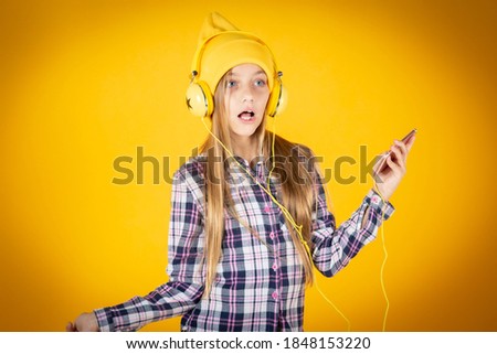 blonde girl listens to music with your cell phone, in yellow background