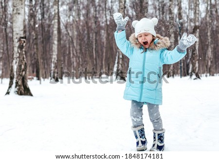 Little girls, sisters are walking, having fun in snowy winter park. Stylish clothes, blue jackets with fur,warm pants with snowflakes,cat-shaped mittens.Family picnic in cold weather.Outdoor activity.