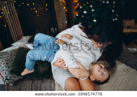 beautiful brown-haired mom and lovely boy son sitting on the floor hugging and playing against the background of the Christmas tree