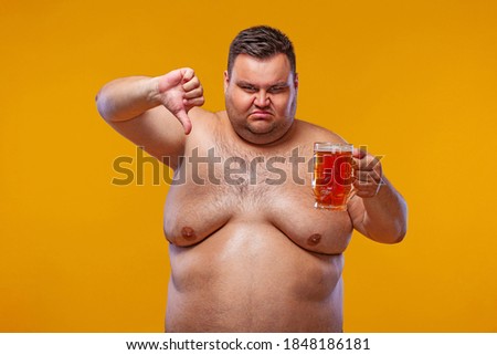 Young fat man at oktoberfest, drinking beer on yellow background. Body positive. Man dislikes beer