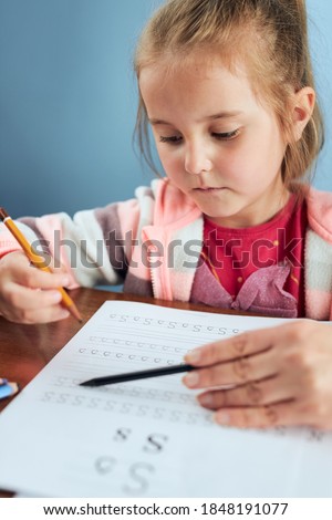 Little girl preschooler learning to write letters with help of her tutor. Kid writing letters doing a school work. Concept of early education