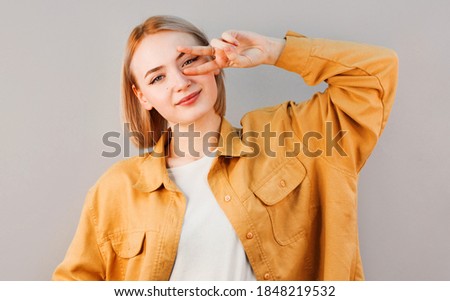 Close up portrait of playful excited funny joyful positive optimistic with toothy smile girl showing v-sign isolated on gray background copy-space