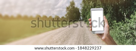 Banner mockup of a smartphone in a girl's hand. Against the background of a field road by the forest