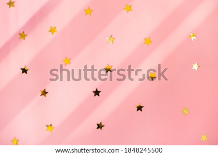 Shiny golden sparkles stars confetti on pink holiday festive background. Top view flat lay for Christmas or Birthday design.